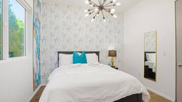 A bedroom with a bed, a nightstand, a lamp, a mirror, and a window.