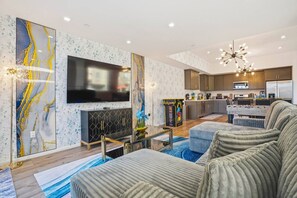 A modern living room with a flat-screen TV, a fireplace, and a kitchen in the background.