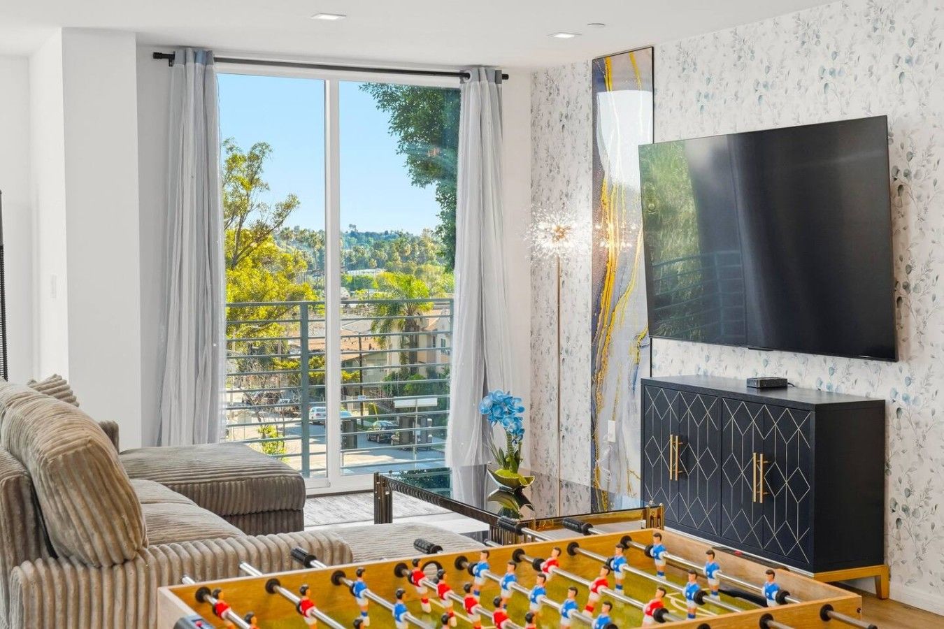 Ein Wohnzimmer mit einer Couch, einem Kicker, einem Fernseher und Blick ins Freie.