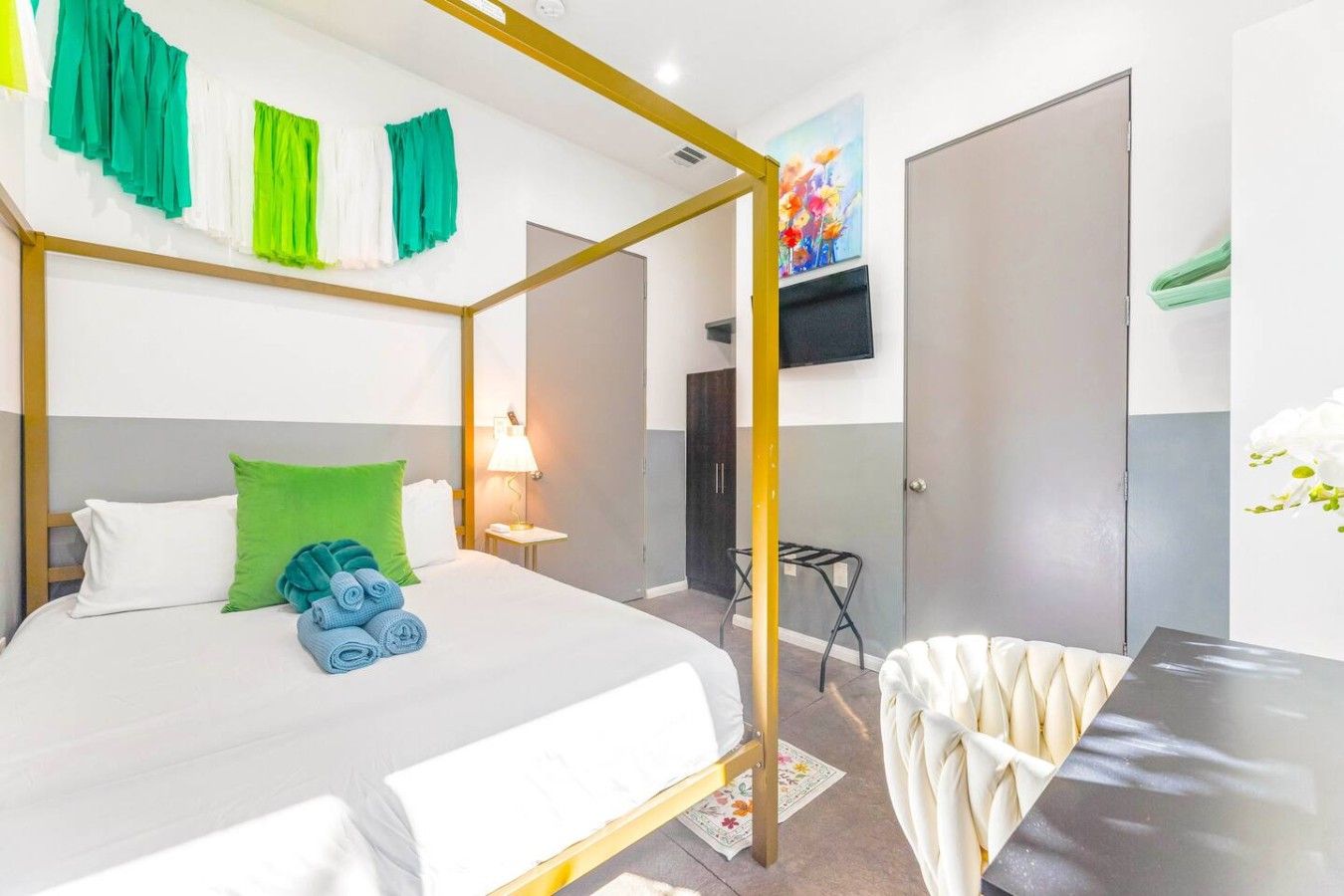 A hotel room with a four-poster bed, a desk, a chair, and a TV mounted on the wall.