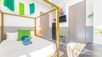 A hotel room with a four-poster bed, a desk, a chair, and a TV mounted on the wall.