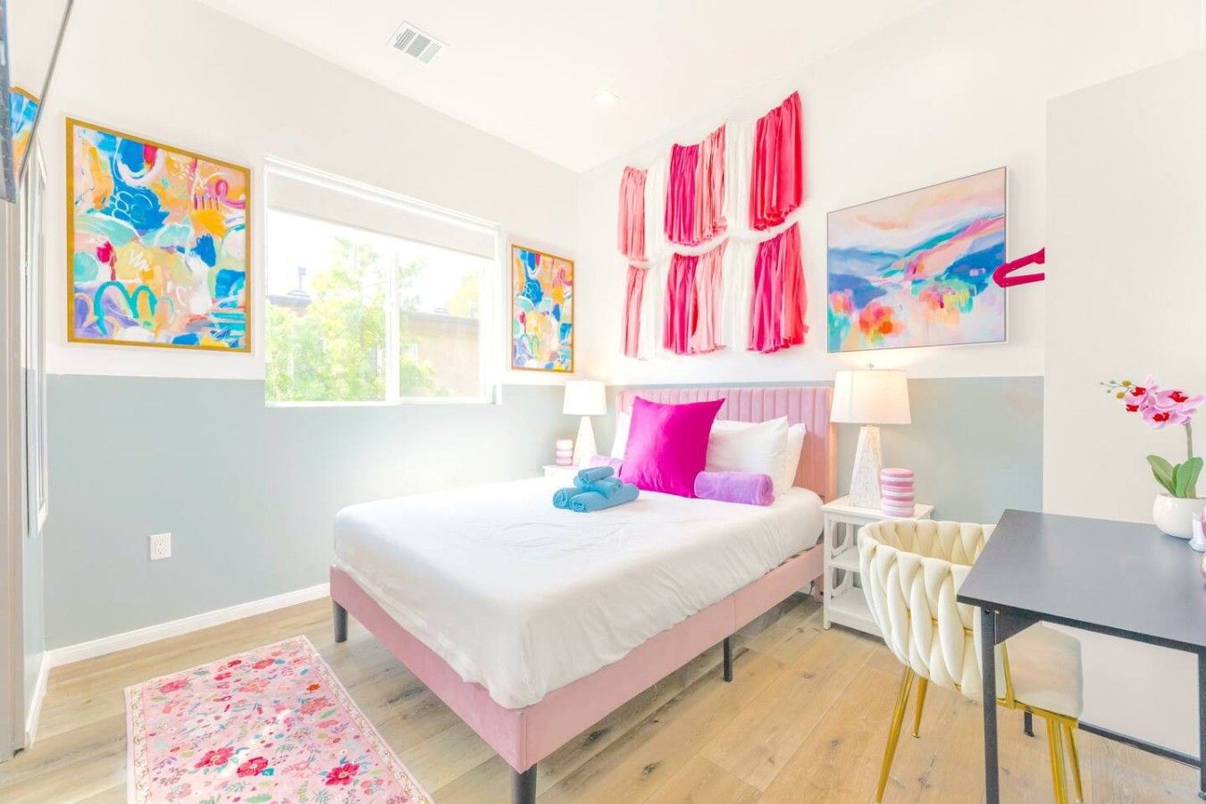 A bedroom with a bed, bedside tables, a desk, and artwork on the walls.