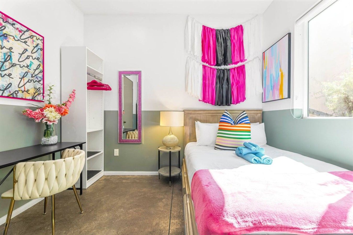 A hotel room with a bed, a desk, a chair, a mirror, and a window.