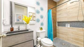 A modern bathroom with a shower, toilet, sink, and a mirror.