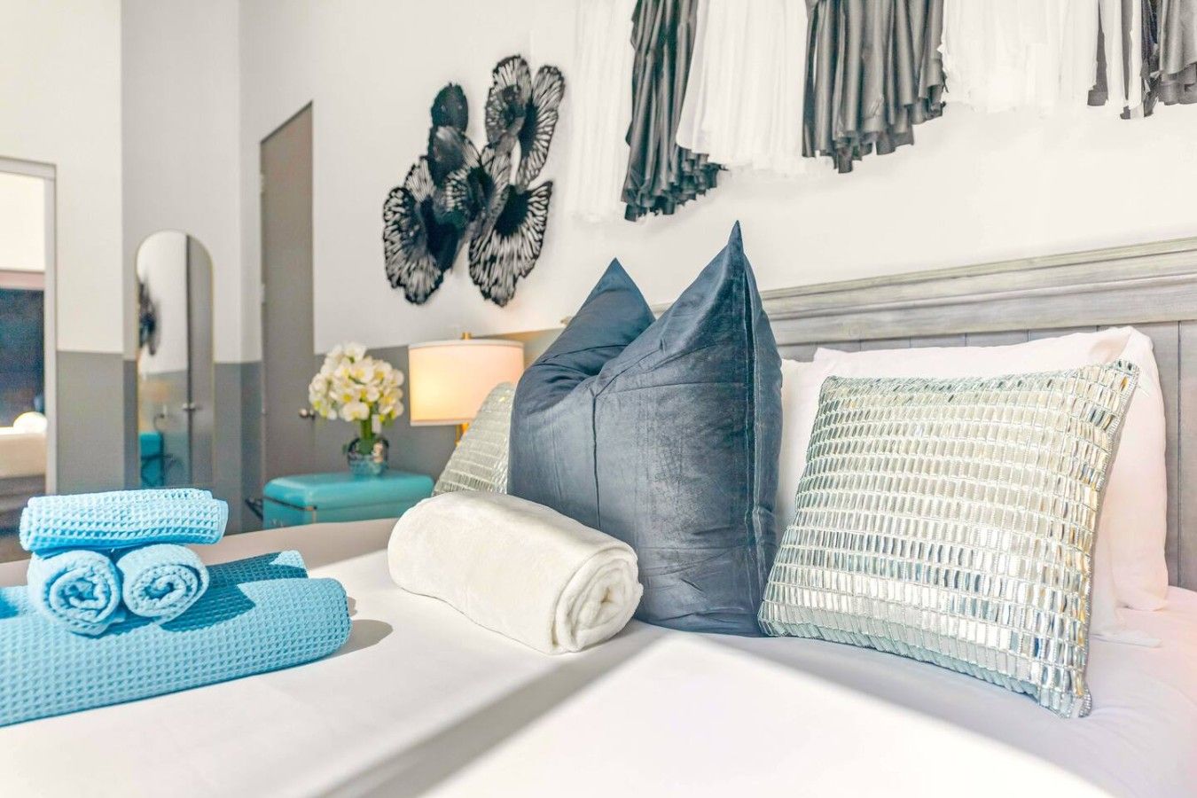 A neatly made bed with pillows and rolled towels, a mirror, and wall art.