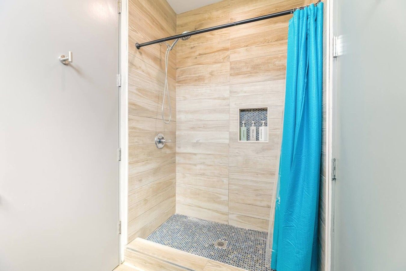A shower with a wooden wall, a metal showerhead, and a blue shower curtain.