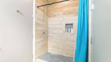 A shower with a wooden wall, a metal showerhead, and a blue shower curtain.