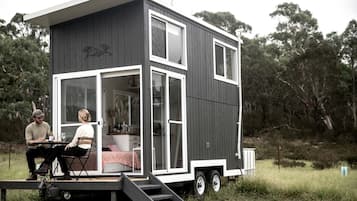 Una pequeña casa moderna de dos pisos con un balcón y un porche, que cuenta con una zona de cocina y un espacio para sentarse.