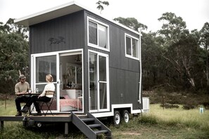 En moderne, tossetagers minihus med en terrasse og en lille veranda, der har et køkkenområde og et siddeområde.