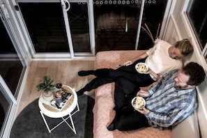 A room with a sofa, a small table with a plant, and a window with a view.