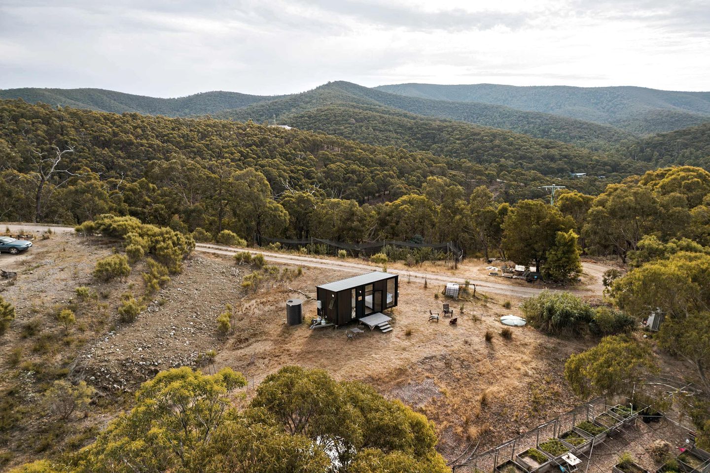 A remote cabin with a dirt ground, surrounded by dense forest and hills.