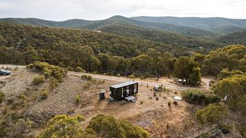 A remote cabin with a dirt ground, surrounded by dense forest and hills.