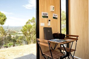 A room with a wooden desk, a laptop, and a bench. There are signs on the wall indicating temperature and energy-saving tips. - Elevated Tiny House with Valley and Vineyards Views in Victoria (Steels Creek)