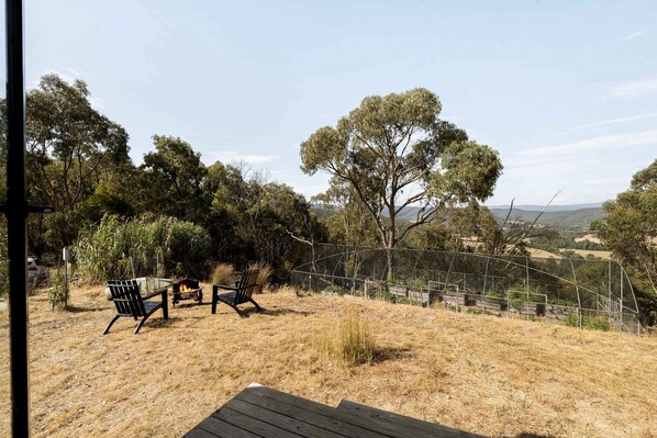 A fenced outdoor area with two chairs and a fire pit, surrounded by trees and a hilly landscape. - Elevated Tiny House with Valley and Vineyards Views in Victoria (Steels Creek)