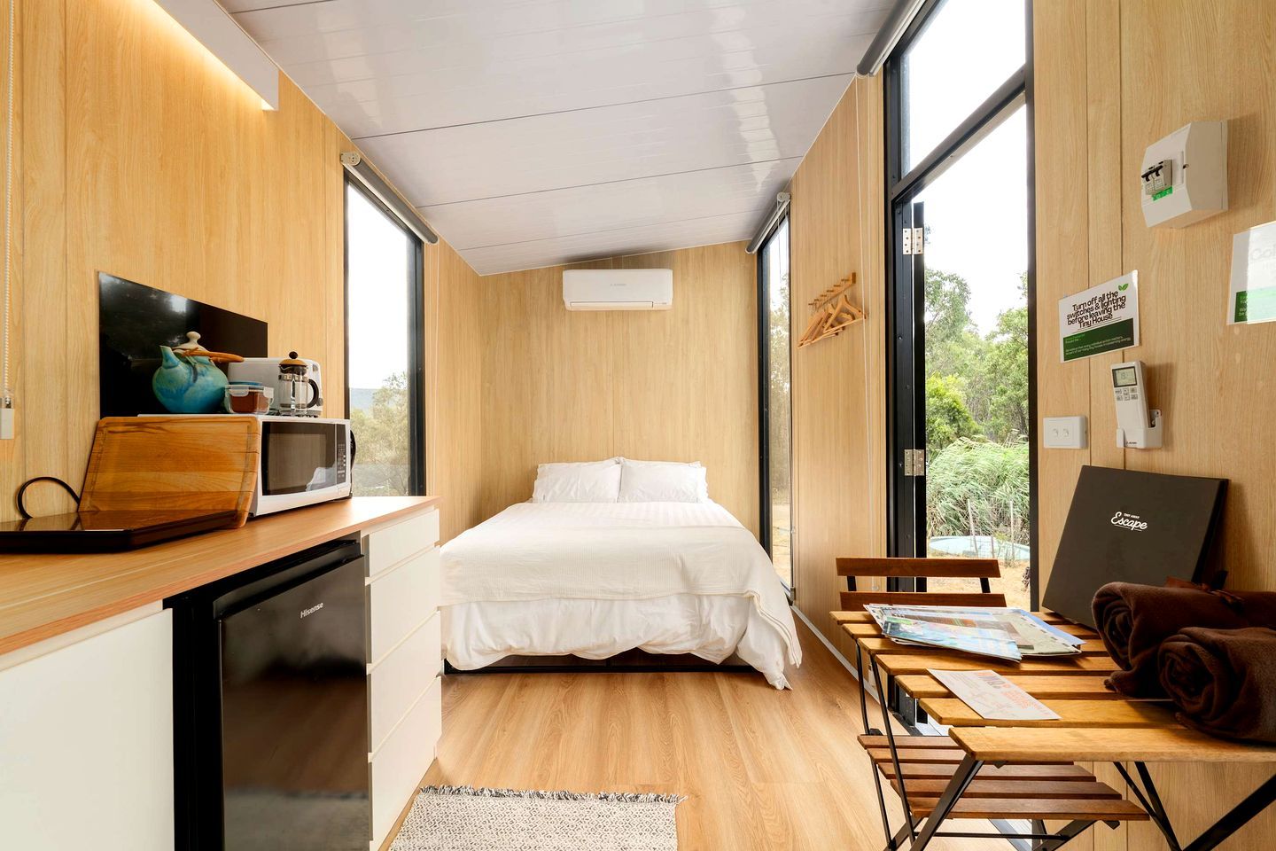 Een compacte kamer met een bed, een kleine kitchenette, een eethoek en een groot raam met uitzicht op de omgeving.