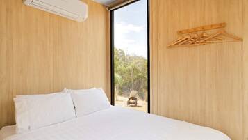 Een slaapkamer met een groot bed, houten wanden, een raam en een rek voor kleding.