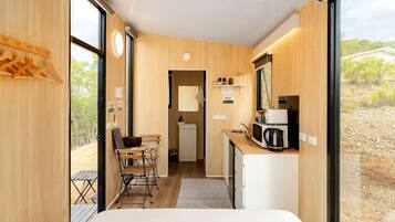A compact room with a bed, a desk, a chair, a small kitchenette, and a view of the outdoors.