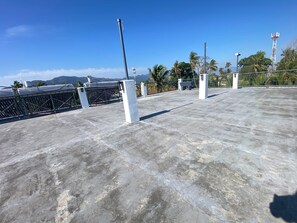 Terraço com piso de concreto, grades de metal e vista ampla de palmeiras e montanhas ao fundo.