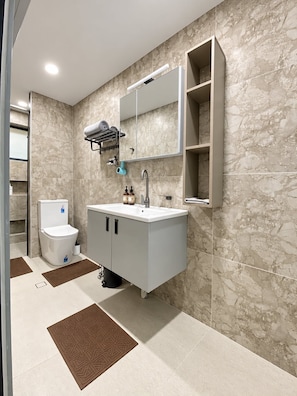 A modern bathroom with a marble wall, a white sink, a toilet, and a towel rack. - 2-bedroom apartment in peaceful Nasoso Nadi with AC comfort (Nasoso Nadi)