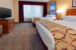 Habitación de hotel con dos camas, un televisor, un aparador y una ventana con cortinas.