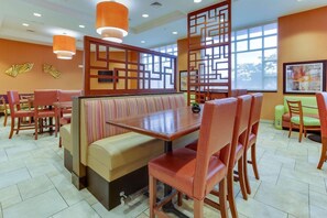 Un restaurante con zona de mesas, sillas de madera y un amplio ventanal que proporciona luz natural.