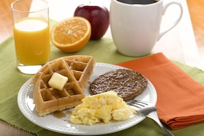Ein Teller Frühstück mit Waffeln, Rührei und einer Frikadelle, dazu ein Glas Orangensaft und eine Tasse Kaffee.