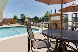 Un área junto a la piscina con sillones de descanso, una mesa y sombrillas.