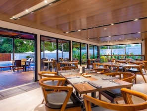 A restaurant with multiple tables and chairs, large windows, and a pool area visible through the glass doors. - Meridian Adventure Marina Club and Resort (Waisai)