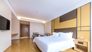 Quarto de hotel moderno com uma cama grande, mesas de cabeceira, televisão de tela plana e um espaço de estar com sofá e mesa.