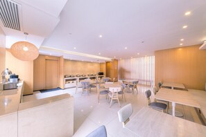 Ein moderner Essbereich mit Tischen und Stühlen, im Hintergrund eine Küche und eine Decke mit Einbautenleuchten.