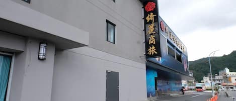 Un edificio con un gran letrero con caracteres chinos, fachada plana y un área de estacionamiento delimitada con conos de tráfico naranjas.