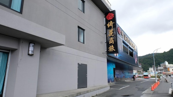 Um edifício com uma grande placa com caracteres chineses, fachada plana e área de estacionamento com cones de trânsito laranja.
