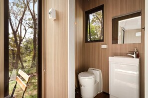 A bathroom with a toilet, sink, and mirror, with a view of trees through a window.