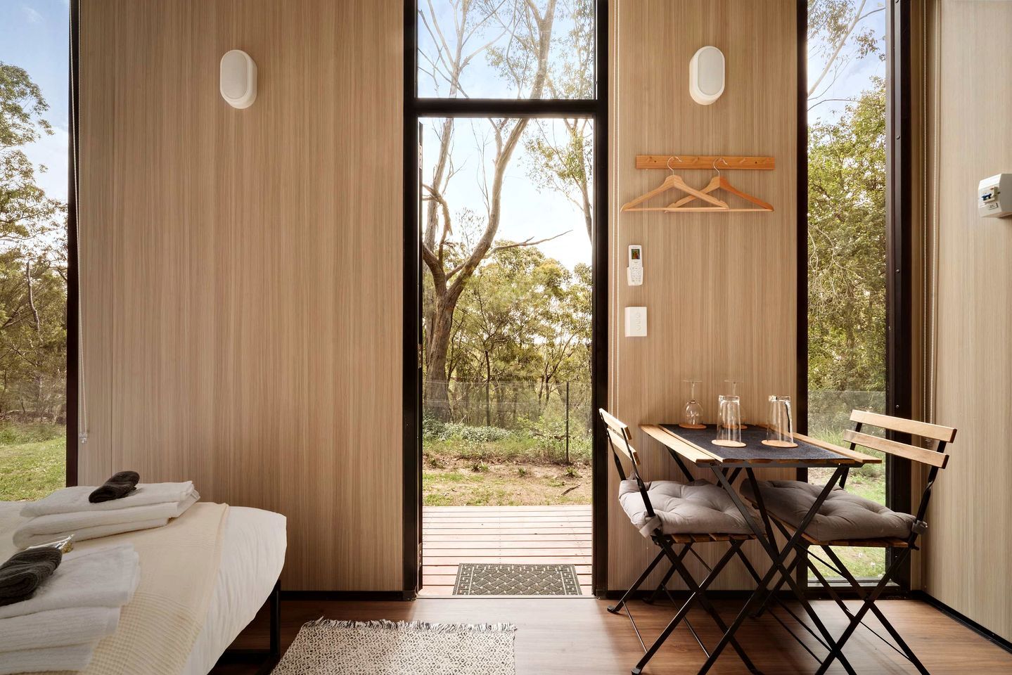 A modern room with a bed, a table with chairs, and a view of the outdoors through large windows.