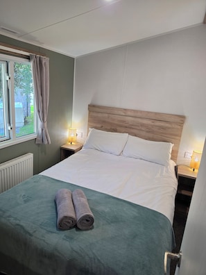 Ein ordentlich bezogenes Bett mit einem Holz-Kopfstück, zwei Nachttischlampen und einem Fenster mit Vorhängen.