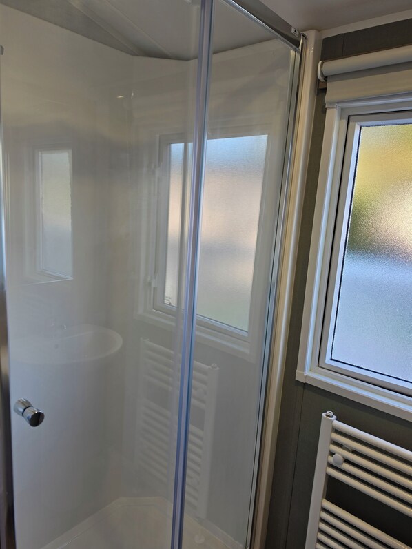 Ein Badezimmer mit Duschkabine aus Glas, einem weißen Heizkörper und einem Fenster mit Milchglas.