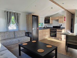 Ein modernes Wohnzimmer mit einer Couch, einem Esstisch mit Korkauflage, einer Küche mit Holzschränken und einer Mikrowelle.