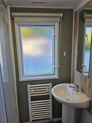 Un baño con ventana, un lavabo blanco y un perchero para toallas.