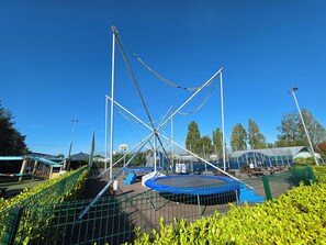 Ein Spielplatz im Freien mit Trampolin, Klettergerüsten und einem Basketballkorb.