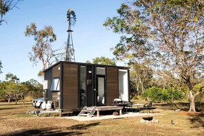 A small, modern cabin with a metal windmill, a picnic table, and a grill area.