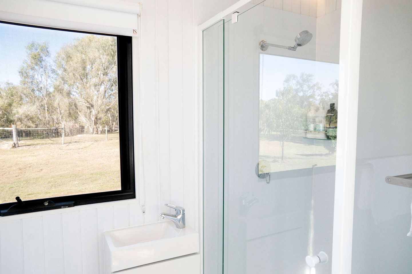 A bathroom with a window, a sink, and a glass shower enclosure.