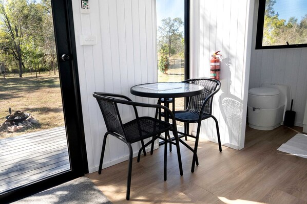A room with a round table and two chairs, a fire extinguisher, and a view of the outdoors.