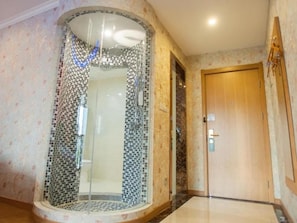 Quarto com área de chuveiro revestida em mosaico, porta de madeira e chão em azulejo.