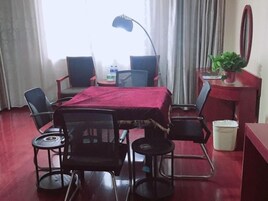 Habitación de hotel con una mesa de comedor, sillas, un escritorio, una lámpara, un espejo y una planta en maceta.