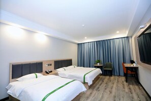 Quarto de hotel com duas camas, uma escrivaninha, uma cadeira, uma mesinha com uma planta e uma janela com cortinas.