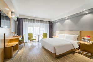 Ein Hotelzimmer mit Bett, Schreibtisch, Stuhl, Fernseher und einem Fenster mit Vorhängen.