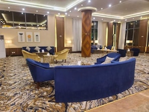 A hotel lobby with a marble-patterned carpet, a large wooden pillar, and seating arrangements including sofas and armchairs. - Anova Hotel (Riyadh)