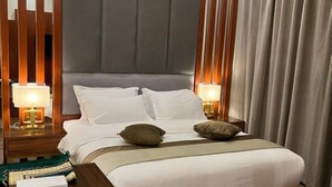 A modern hotel room with a large bed, wooden headboard, two bedside tables with lamps, and a large window with curtains. - Anova Hotel (Riyadh)