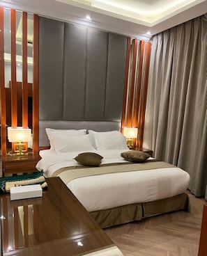 A modern hotel room with a large bed, wooden headboard, two bedside tables with lamps, and a large window with curtains. - Anova Hotel (Riyadh)