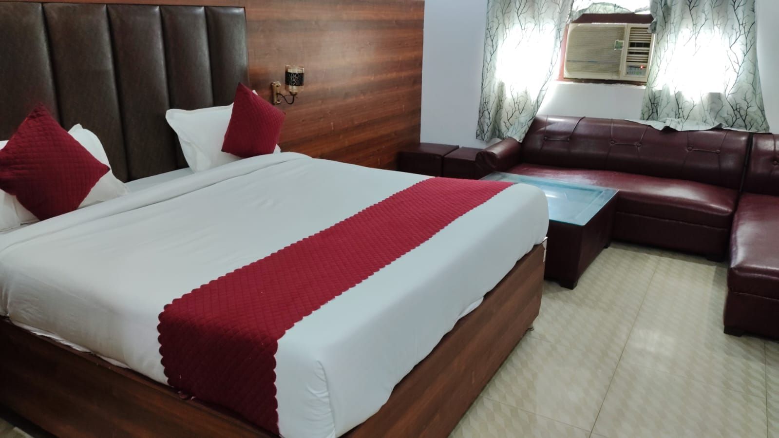 A hotel room with a bed, a sofa, a small table, and a wall-mounted lamp.